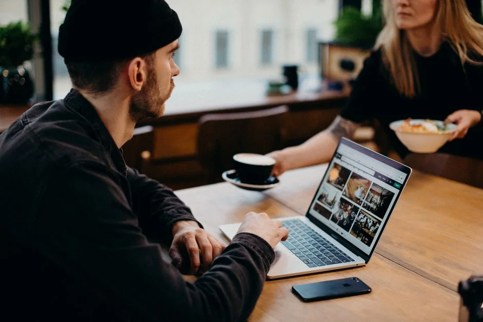 Gros plan sur des mains qui tapent sur un ordinateur portable, à côté d’une tasse de café posée sur un bureau en bois.